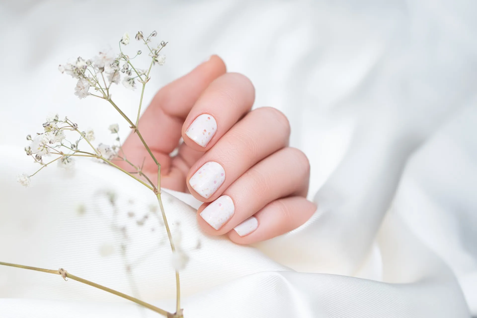 A flawless white manicure resting on satin with baby’s breath