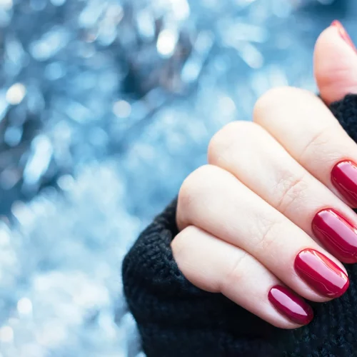 Hand with red manicured nails over blue background.