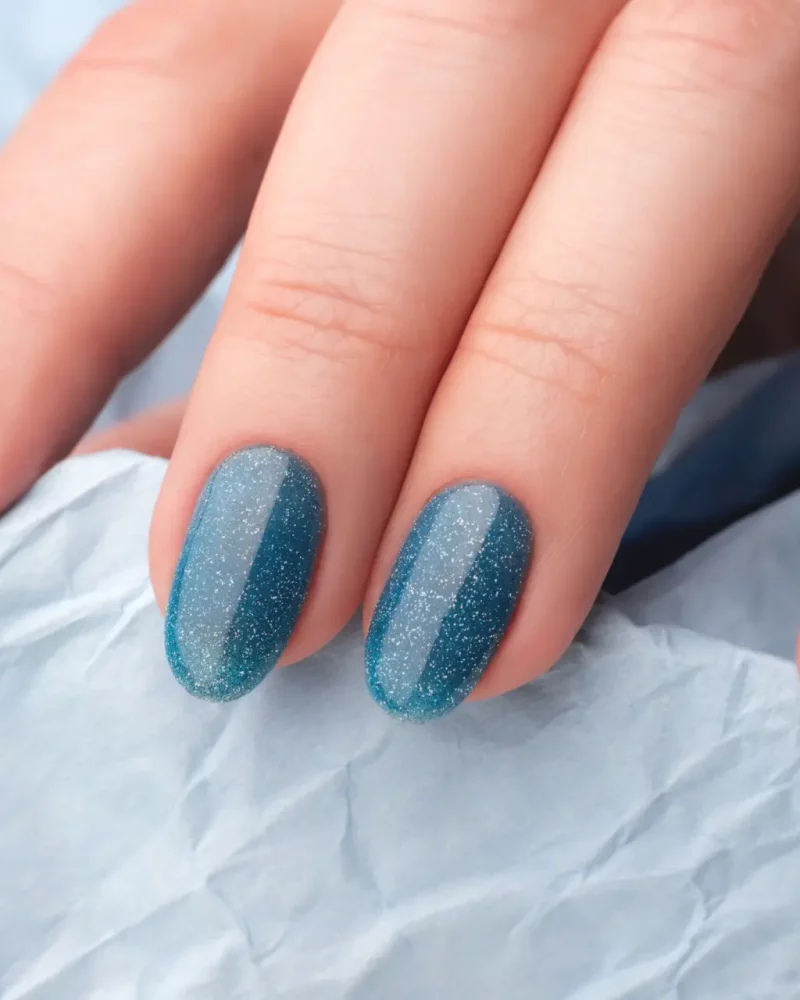 Glittery blue nail polish on fingernails.