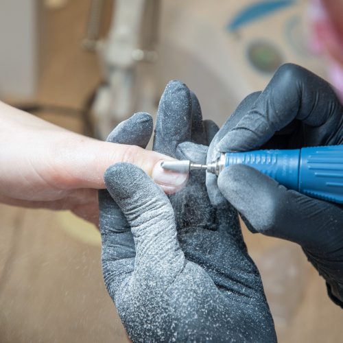 The manicurist grinds off the old coating with professional electric nail file.