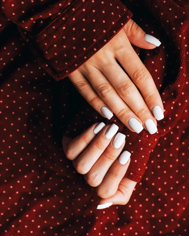 Woman's hands with white manicure on red polka dot fabric.