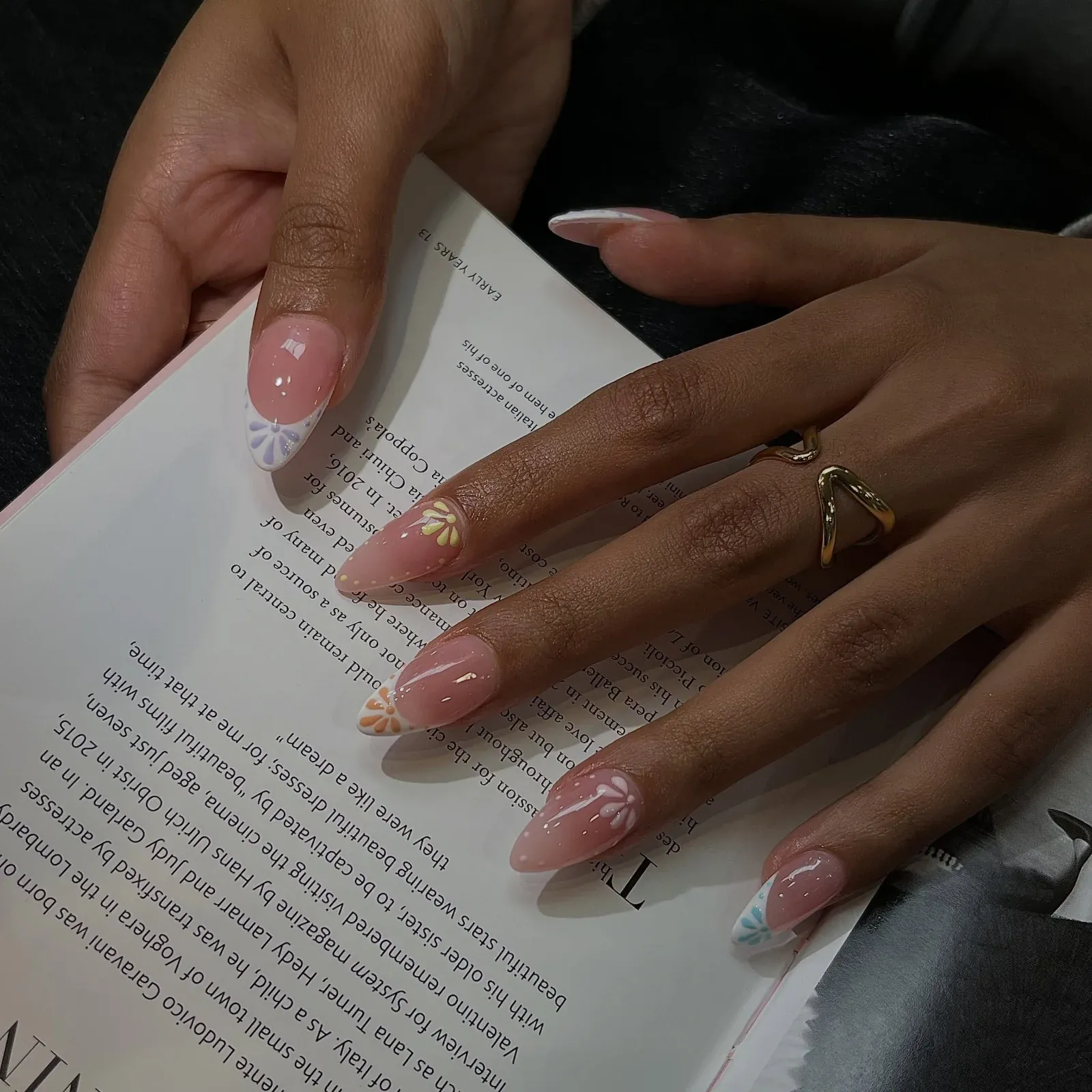 A sheer nude manicure with fine painted detail, hands resting on an open book